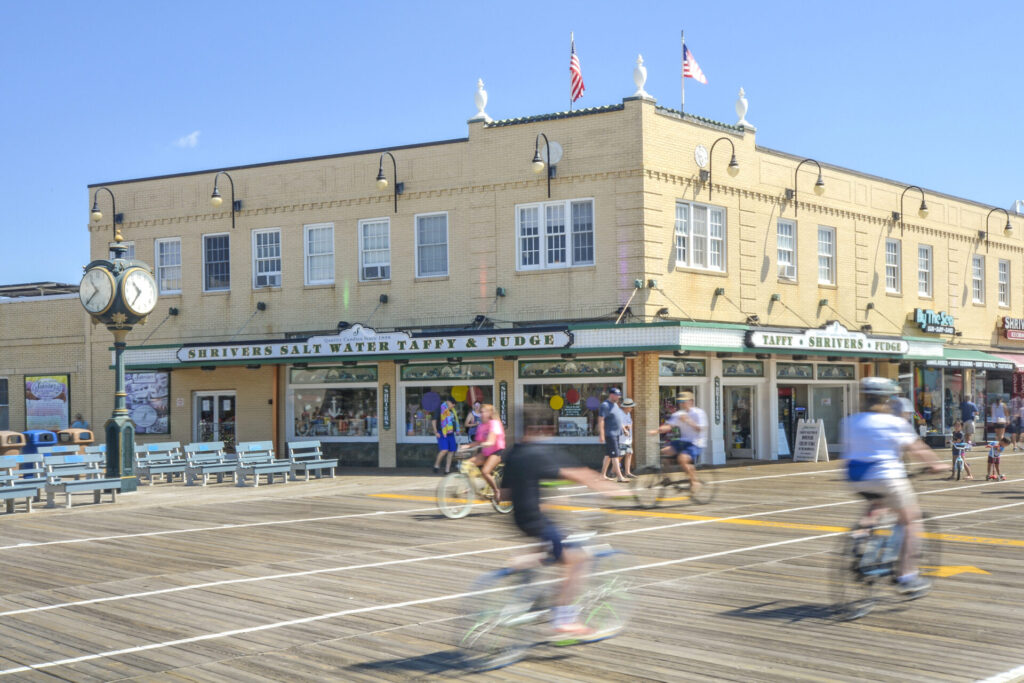 Several people biking on the Ocean City Boardwalk in front of a large yellow building